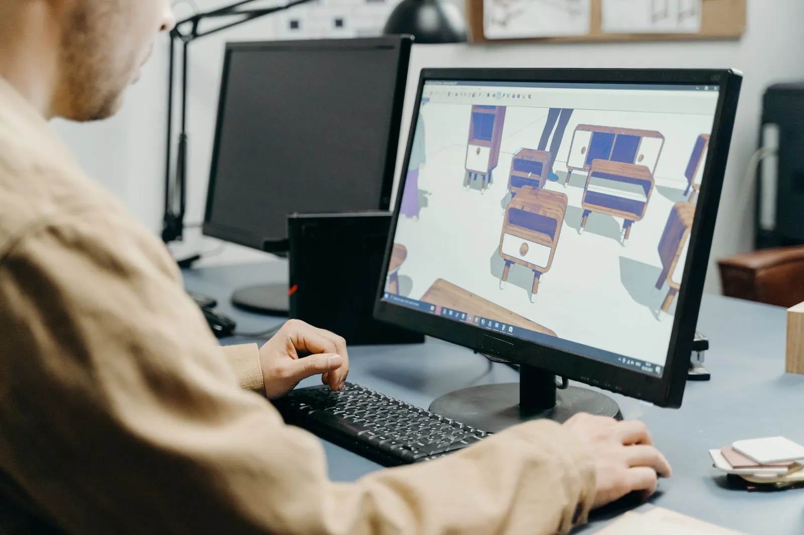 A designer building 3D furniture models of an office layout on a computer