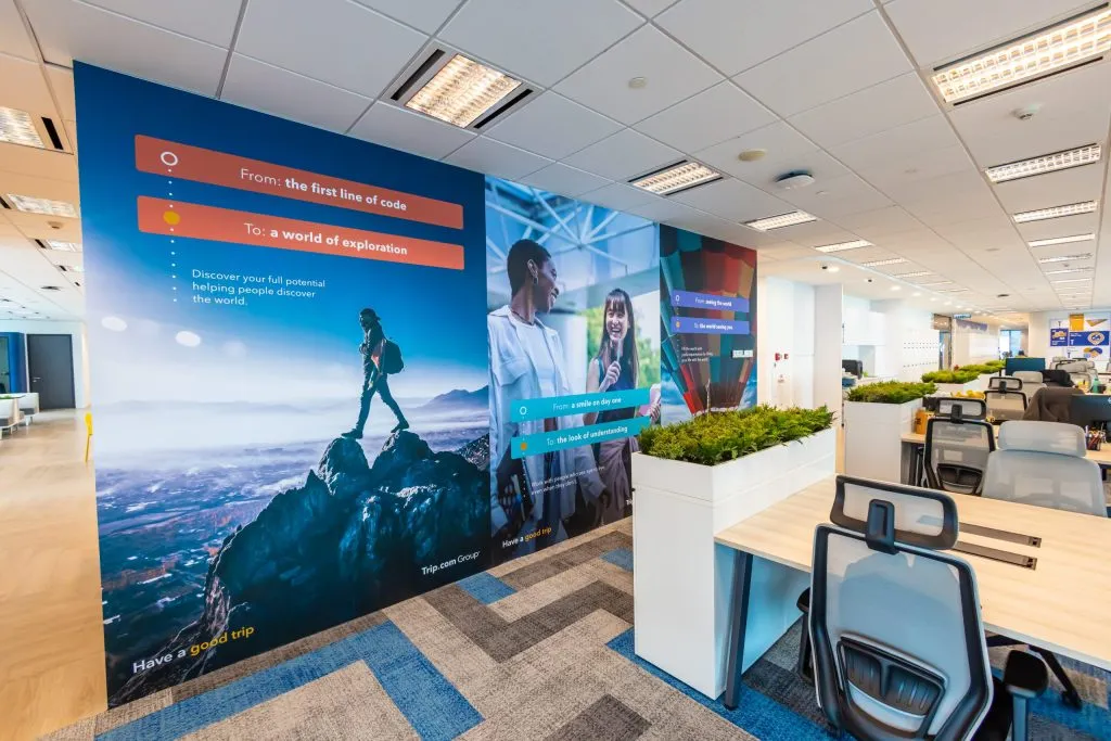Open-plan office with a large brand mural wall and planter dividers