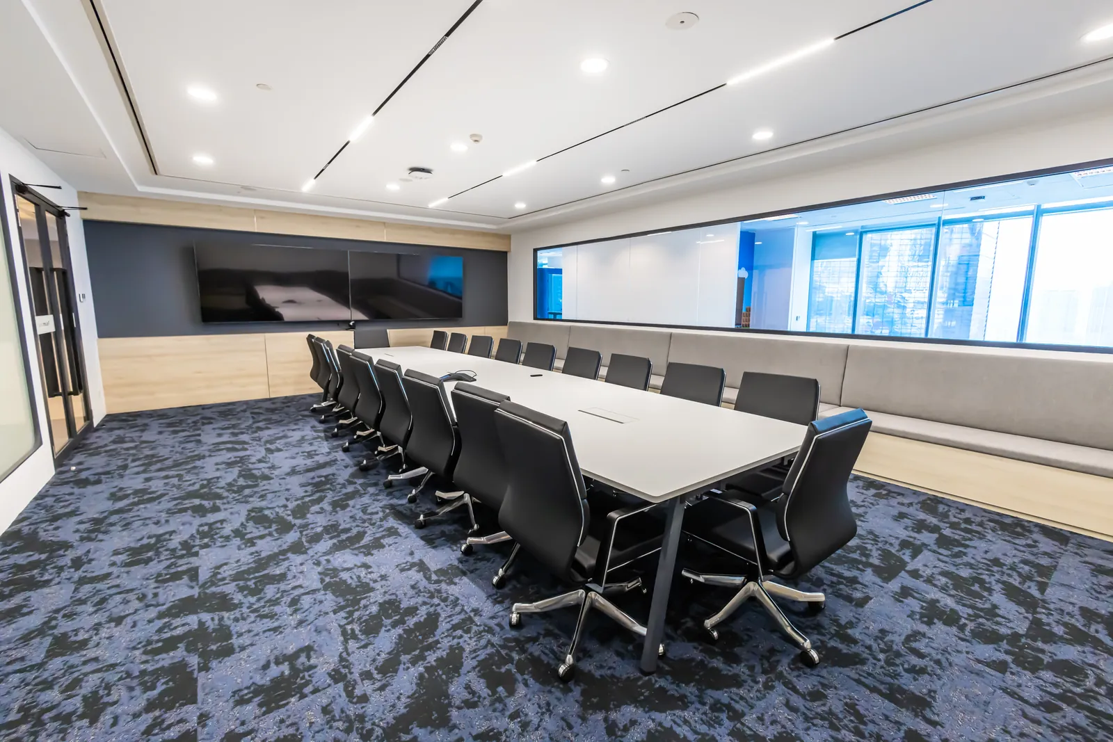 Long boardroom with a video wall, full-height windows and patterned carpet