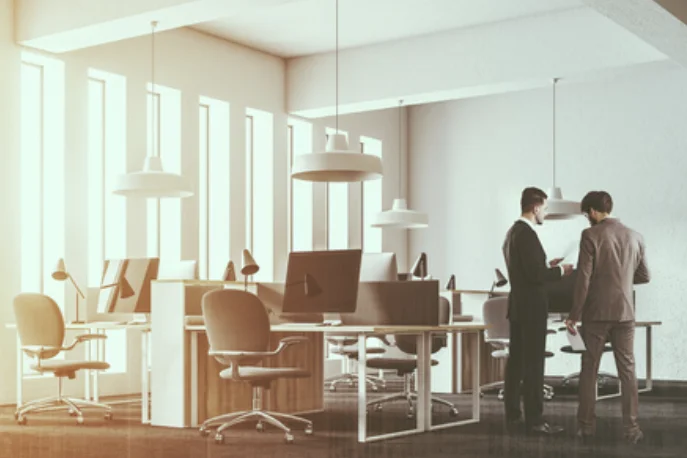 Two colleagues talking beside rows of open-plan workstations